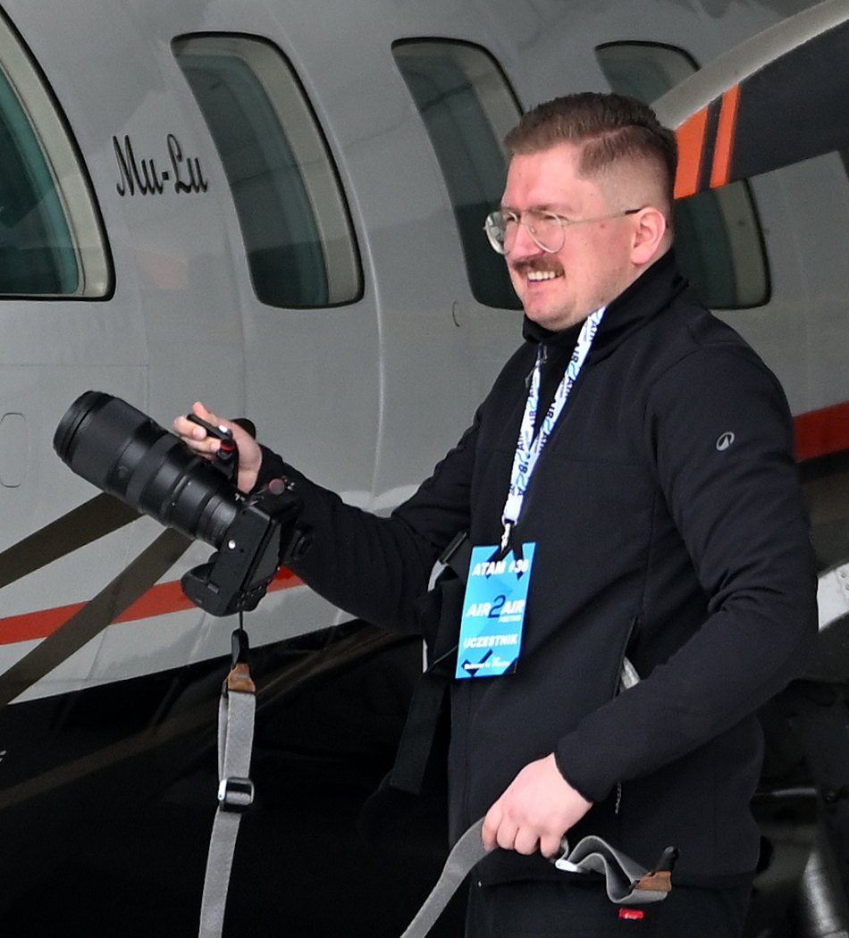 Przemek in a hangar, laughing, a telephoto in one hand