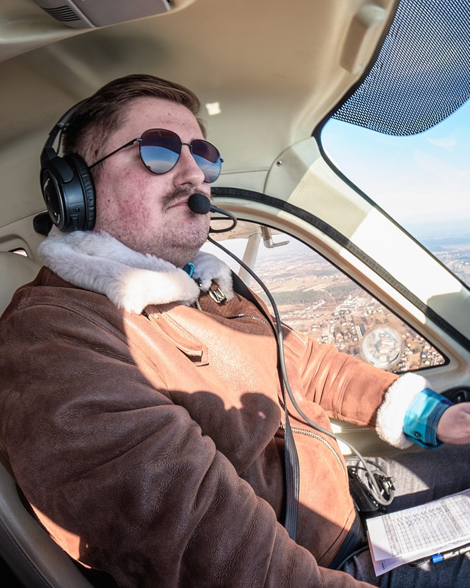Przemek in the left seat, headset on, the ground turning under the windscreen